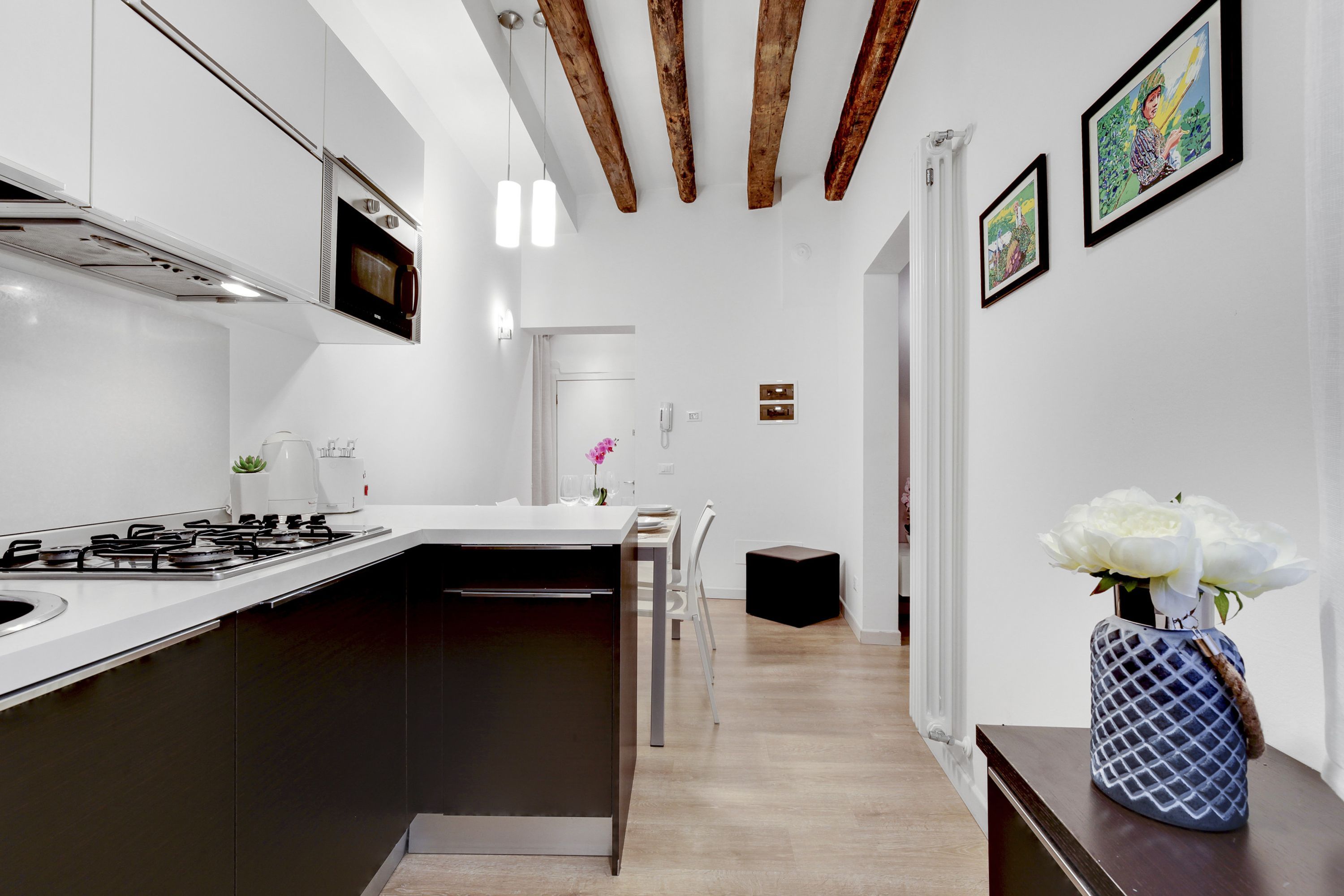 Una cocina moderna con una isla central, microondas y estufa. Hay un pasillo que lleva a otra habitación con una puerta y un taburete pequeño.