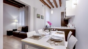A dining area with a table set for four, a sofa, a lamp, and a kitchen in the background. - Ca dei Botteri 2 by Wonderful Italy (Venice)