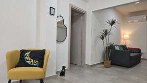 Ein modernes Wohnzimmer mit einem gelben Sessel, einem grauen Sofa und einem kleinen Hund. An der Wand hängt ein Spiegel, es gibt eine Pflanze und eine Lampe.