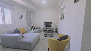 A modern living room with a grey sectional sofa, a yellow armchair, a coffee table, and a flat-screen TV. - 148 Lim- Stay Synergy House (Limassol)