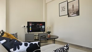 Ein modernes Wohnzimmer mit Flachbildfernseher, Couchtisch und Sofa. An der Wand hängen zwei gerahmte Bilder und auf dem Couchtisch steht eine kleine Topfpflanze.