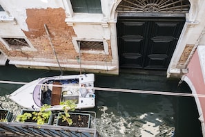 A narrow canal with a boat docked on the left, a black door on the right, and a building with exposed brick and peeling paint.