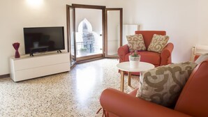 A living room with a television, a sofa, a coffee table, and a view of a building through an open door. - Sansoni Palace by Wonderful Italy (Venice)
