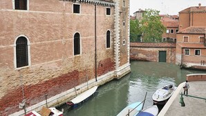 A canal with boats docked, a historic building with a tower, and a bridge. - Ca Vivaldi by Wonderful Italy (Venice)