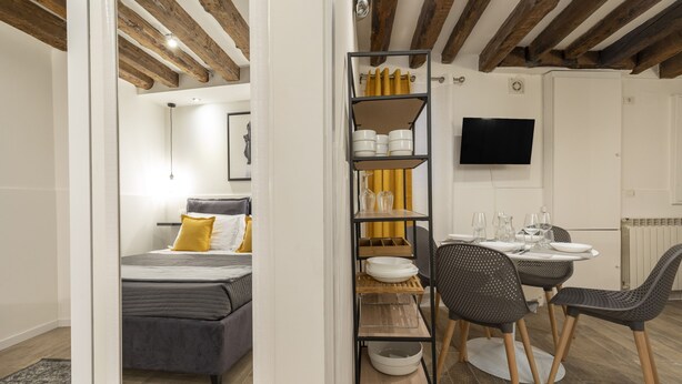 A modern hotel room with a bed, a dining area with a table and chairs, a TV mounted on the wall, and a wooden ceiling. - Accademia II by Wonderful Italy (Venice)