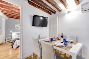 Egy modern étkező, egy fehér, két személyre megterített asztallal, a falra szerelt, síkképernyős televízióval és a mennyezetben látható, nyers fa gerendákkal.