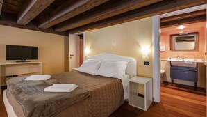 Ein Hotelzimmer mit Bett, Nachttisch, Fernseher und einem Badezimmer mit Waschbecken und Spiegel.