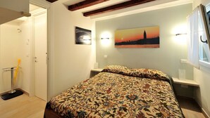 A bedroom with a bed, a painting of a sunset, and a window with curtains.