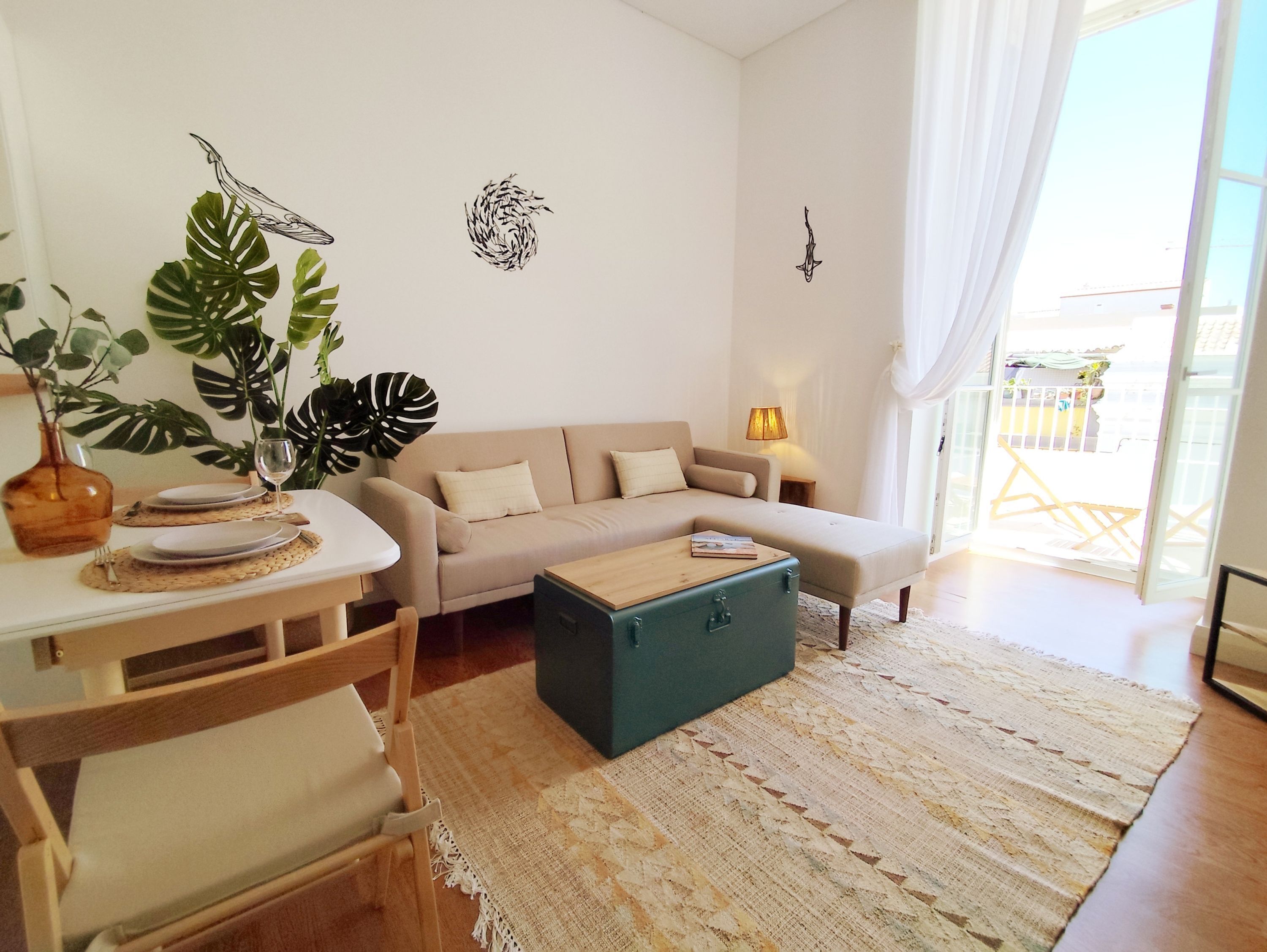 Un salón con sofá, una mesa de centro y una mesa de comedor dispuesta con platos y una copa. Hay plantas y decoración en las paredes.
