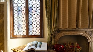Ein Zimmer mit Schreibtisch aus Holz, einem offenen Buch, einer Vase mit roten Blumen und einem Kamin.