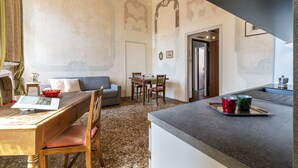Ein Essbereich mit Holztisch, Stühlen und einer Couch. Es gibt eine Küchenzeile mit einer Arbeitsplatte und einer Ablage mit zwei Tassen.