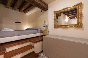 Ein Schlafzimmer mit einem Bett, Holzstufen, einem Schminktisch und einem Spiegel mit aufwendiger Rahmenverzierungen.