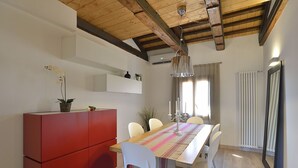 Un comedor con una mesa larga, sillas blancas, un armario rojo y una lámpara colgante.