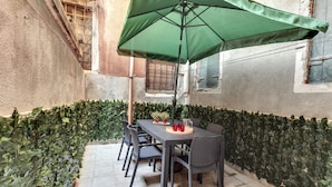 A patio with a table and chairs under a green umbrella, surrounded by a hedge. - Pozzo Roverso by Wonderful Italy (Venice)