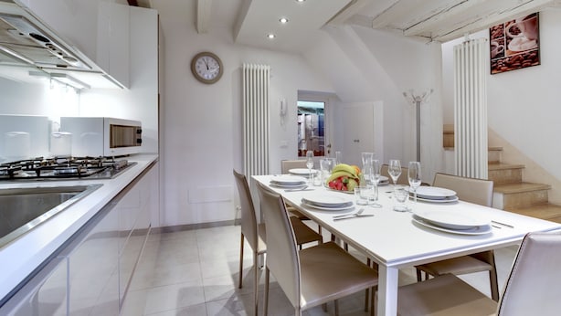 A modern kitchen with a gas stove, white cabinets, and a dining area with a white table set for four. - Pozzo Roverso by Wonderful Italy (Venice)
