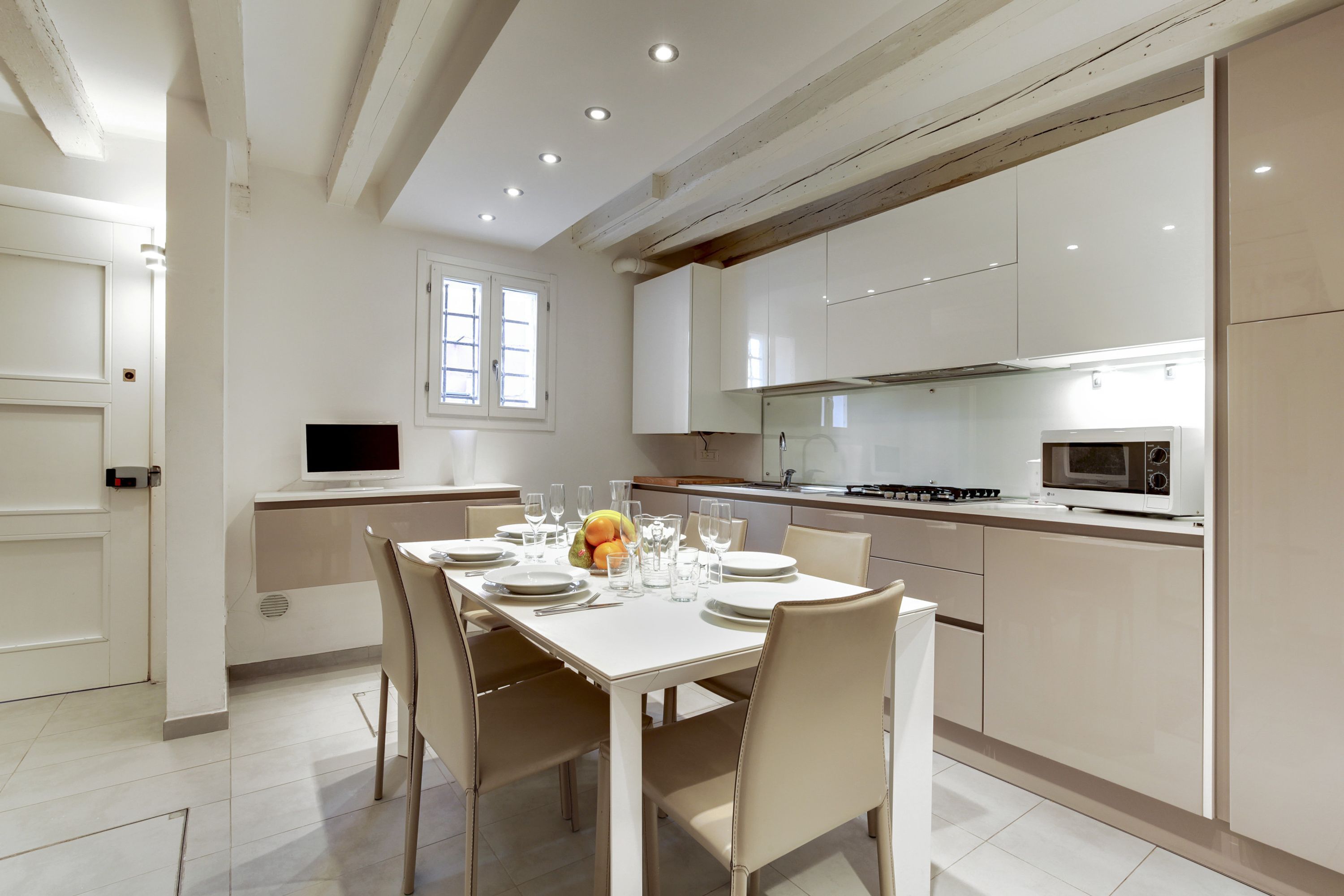A modern kitchen with white cabinetry, a dining table set for four, and a built-in oven.