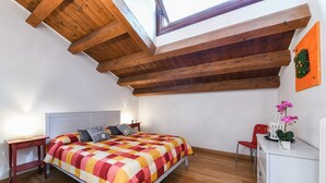 Ein Schlafzimmer mit Holzboden, einem Bett mit kariertem Überwurf, einem Nachttisch, einem Stuhl und einer Kommode.