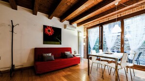 Ein Zimmer mit einem roten Sofa, einem Esstisch mit Stühlen und großen Fenstern mit Vorhängen.