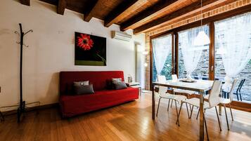 A room with a red sofa, a dining table with chairs, and large windows with curtains.