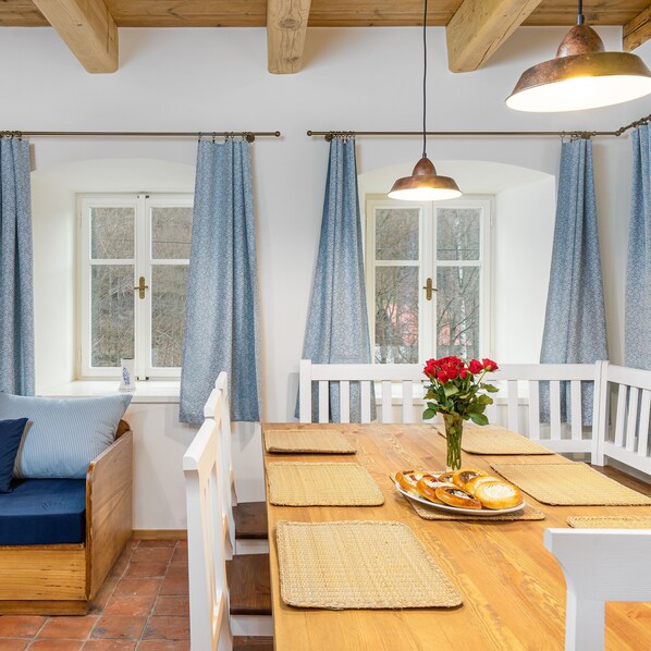 A cozy room with a wooden bench, a dining table with woven placemats, a vase of red flowers, and a view of trees through the window. - Villa met Sauna Ldd032 (Desna)
