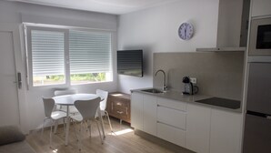 A modern kitchen with white cabinets, a sink, a coffee maker, and a dining area with chairs and a table. - Alén de Louro - Apartamento 1 San Francisco (Lariño)