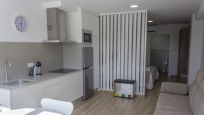 A modern kitchen with white cabinets, a microwave, and a refrigerator. There is a dining area with a white table and chairs. A beige sofa is in the living area. - Alén de Louro - Apartamento 1 San Francisco (Lariño)