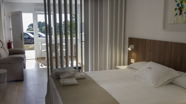 A hotel room with a bed, a sofa, a small table, and a view of the outside. - Alén de Louro - Apartamento 1 San Francisco (Lariño)