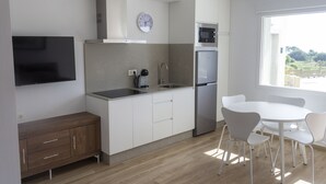 Una cocina moderna con armarios blancos, un refrigerador de acero inoxidable, un microondas y un horno empotrado. Hay una mesa de comedor blanca con sillas y un reloj en la pared.