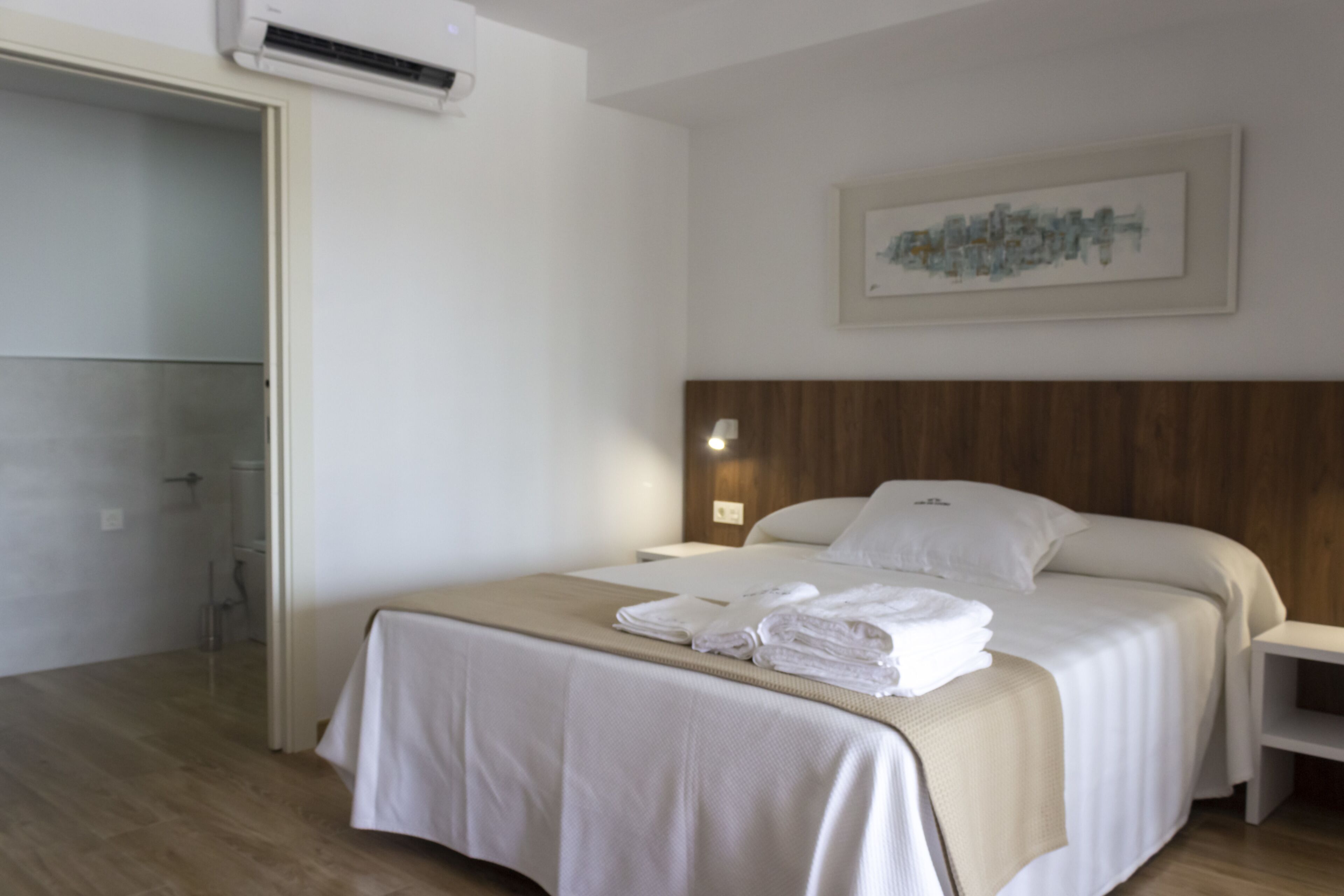 A hotel room with a bed, a nightstand, a wall-mounted lamp, and a painting.