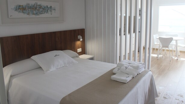 Habitación de hotel con cama, mesita de noche, lámpara de pared, ventana y vistas al exterior.