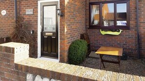 Ein zweistöckiges Ziegelhaus mit Eingangstür, Fenstern und einer kleinen Terrasse mit Tisch und Stühlen.