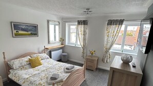 Ein Schlafzimmer mit einem hölzernen Bett, einem Nachttisch, einem Fenster mit Vorhängen und einem Bild an der Wand.