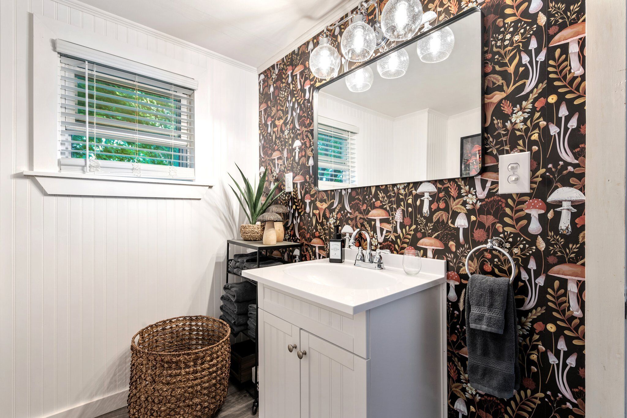 A bathroom with a white vanity, a large mirror, and a wall with a floral pattern.