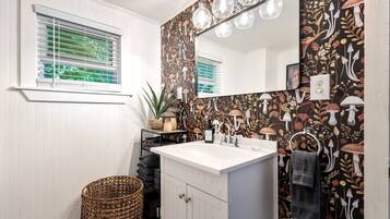 A bathroom with a white vanity, a large mirror, and a wall with a floral pattern.