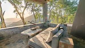 Un espacio al aire libre con pared de piedra, banca de madera y sofá acolchado.