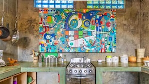 Una cocina con un cuadro abstracto y colorida en la pared, una estufa a gas y diversos utensilios y recipientes de cocina.