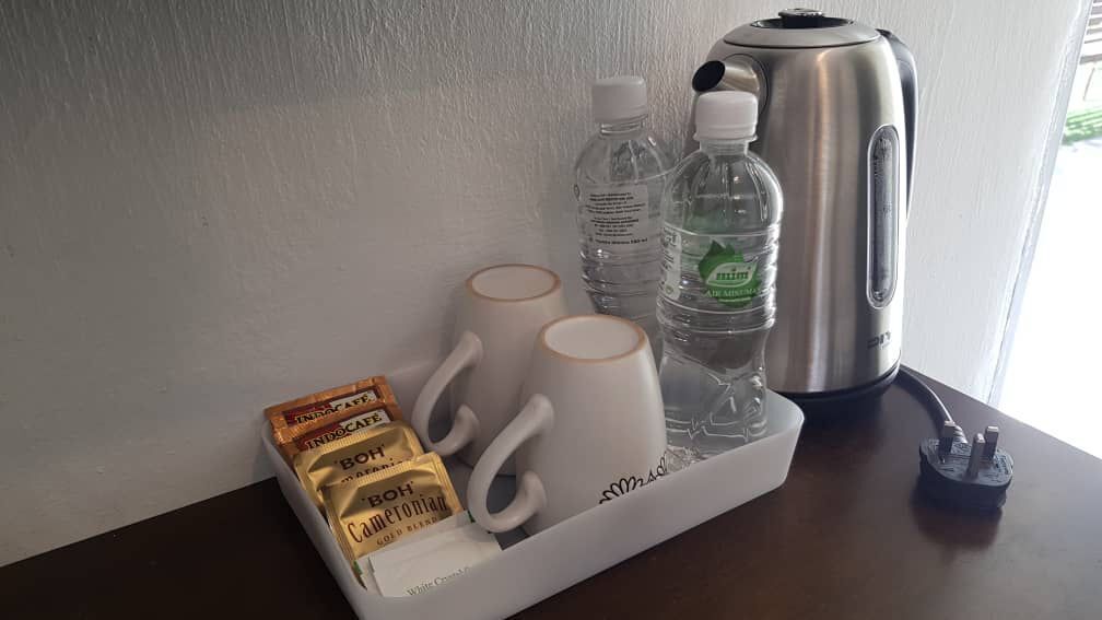 A tray with two white mugs, two bottles of water, a pack of Bohol coffee, and a silver electric kettle on a wooden table.