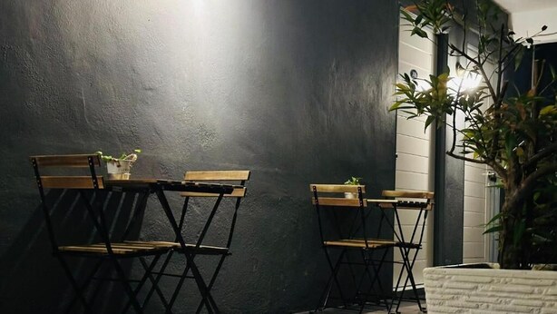 A small outdoor seating area with two wooden chairs and tables, a potted plant, and a textured wall. - Cassa Kaseh Guest House (Langkawi)