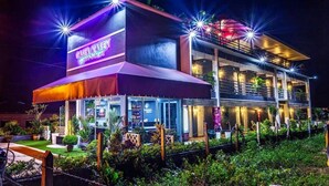 A modern building with a neon sign, multiple balconies, and outdoor seating. - Cassa Kaseh Guest House (Langkawi)