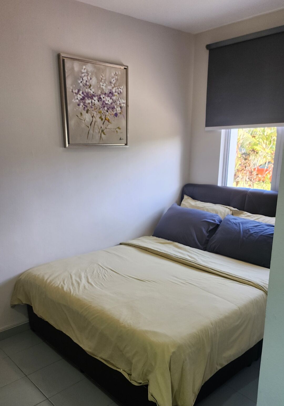 A bedroom with a bed, a window with a view of greenery, and a framed floral artwork on the wall.