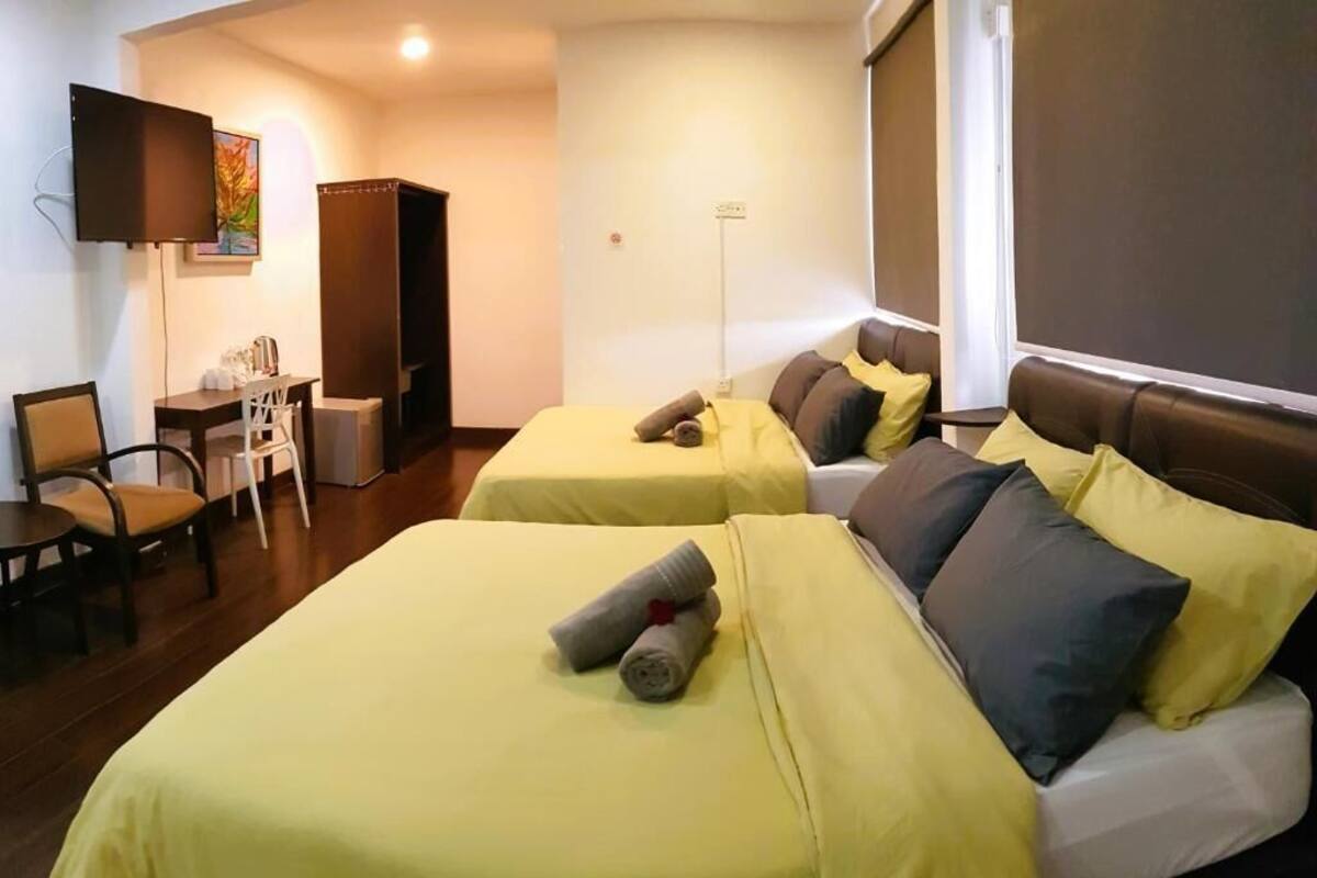 Habitación de hotel con dos camas, un escritorio, una silla y un televisor montado en la pared.