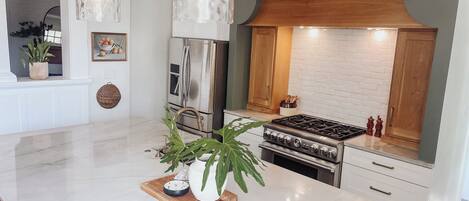 A modern kitchen with a central island, stainless steel appliances, and a white marble countertop.