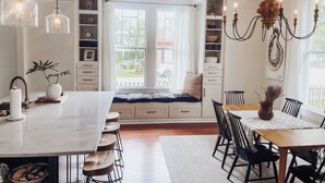 A modern kitchen with a large island, built-in shelves, and a dining area with a bench and chairs. - Guesthouse on Girod (Mandeville)