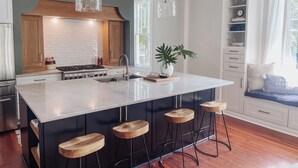 A modern kitchen with a central island, bar stools, pendant lights, and a built-in stove. - Guesthouse on Girod (Mandeville)