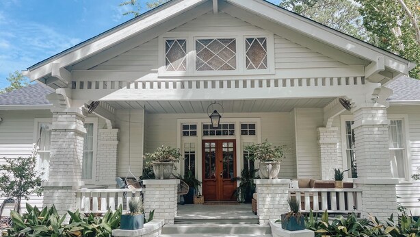A white house with a front porch, steps leading to the door, and potted plants. - Guesthouse on Girod (Mandeville)