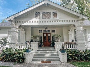 A white house with a front porch, steps leading to the door, and potted plants. - Guesthouse on Girod (Mandeville)