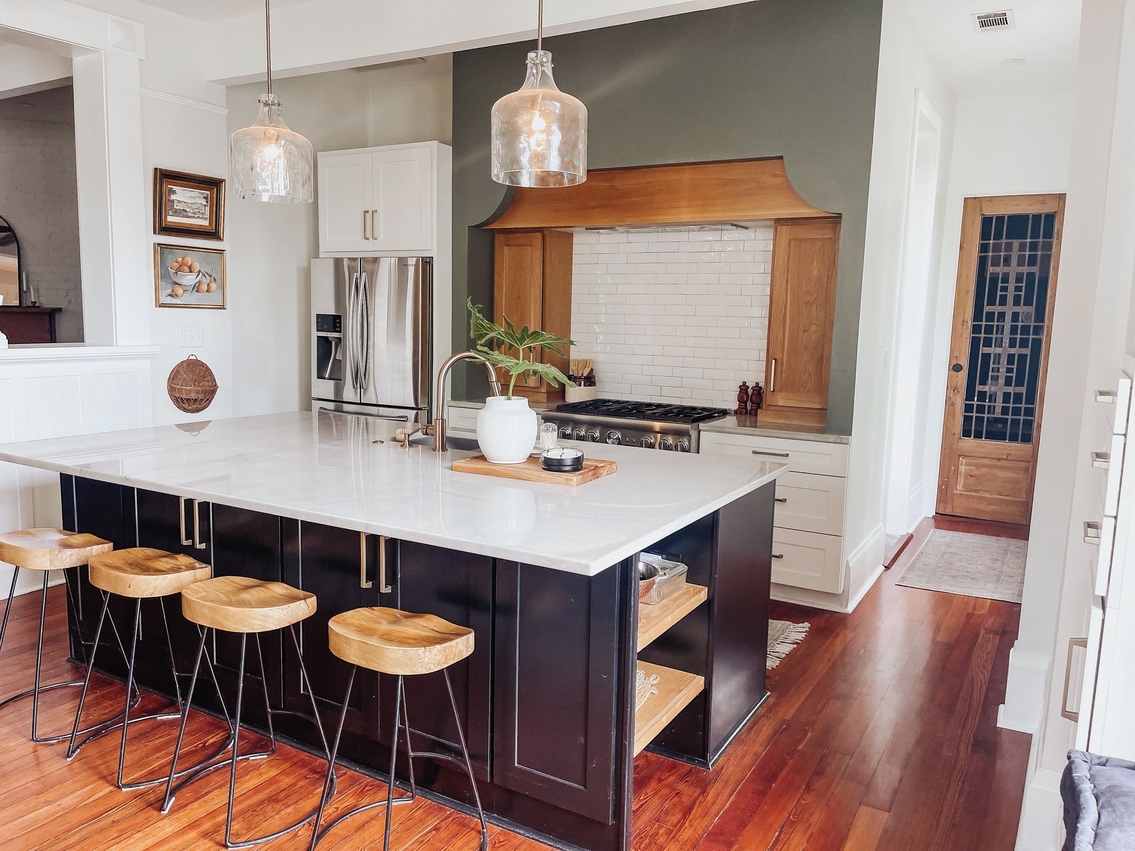 A modern kitchen with a large island, bar stools, stainless steel appliances, and pendant lighting.