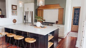 A modern kitchen with a large island, bar stools, stainless steel appliances, and pendant lighting.