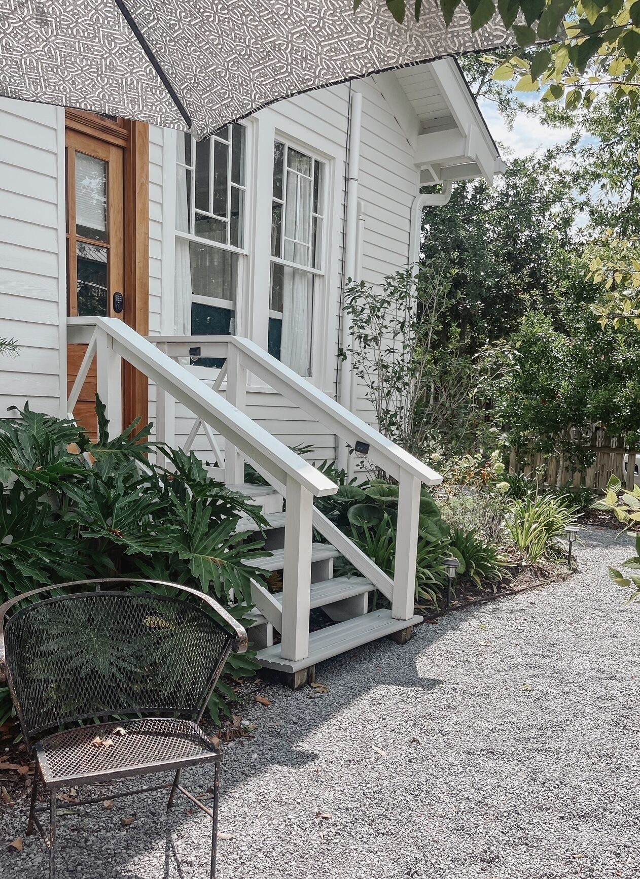 A white house with a wooden door, a white staircase, and a metal chair.