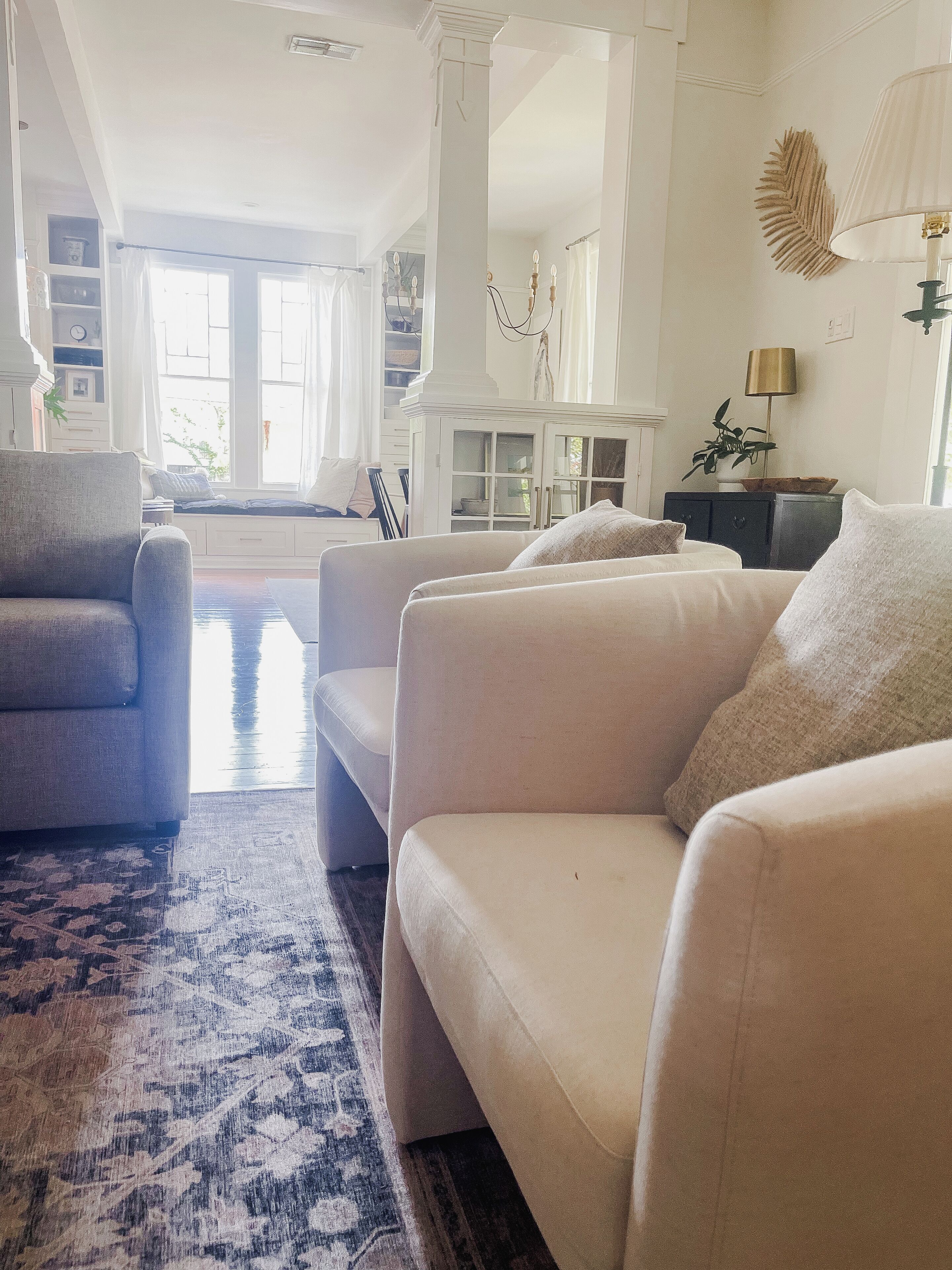 A spacious living room with a large window, a patterned rug, and a modern chandelier.